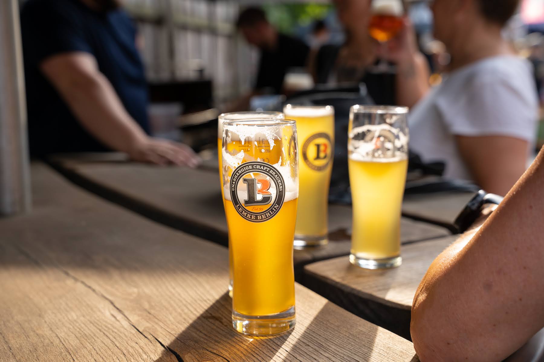 Mehrere gefüllte Biergläser stehen auf einem Biergarten-Tisch und werden von der Sonne erleuchtet.